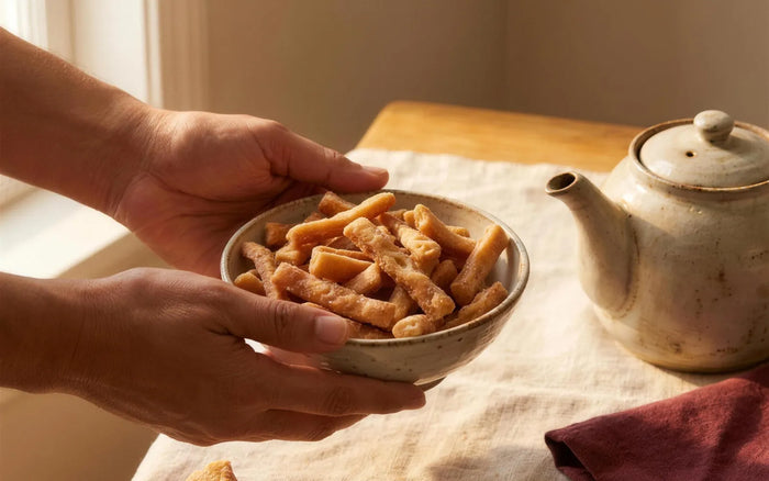 Discover hub card — Story of Kurma: olive-skinned hands sharing a bowl of golden sugar-glazed Kurma