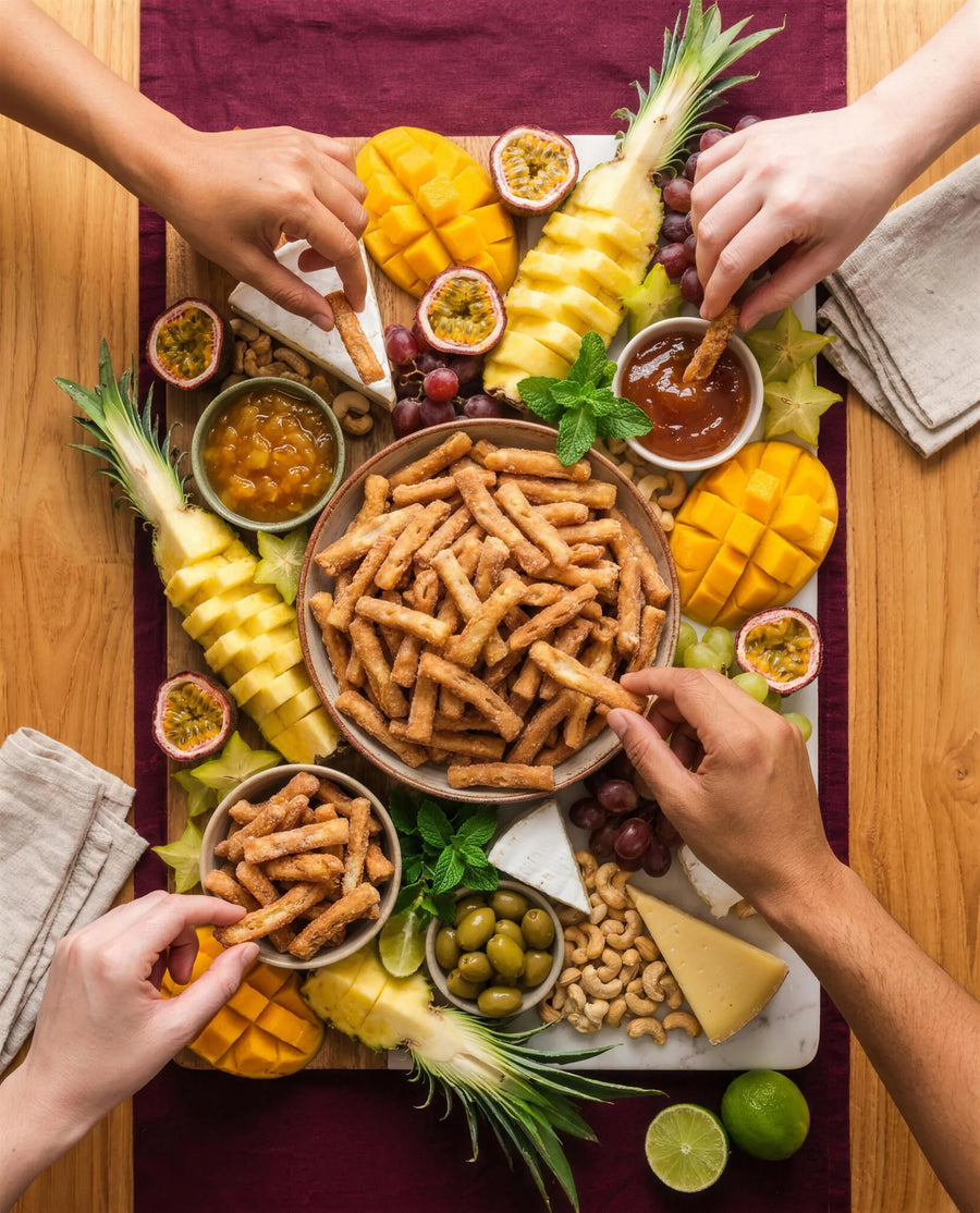 Overhead grazing board with bowls of Kurma at the centre, tropical fruit, cheeses and chutneys, hands reaching in